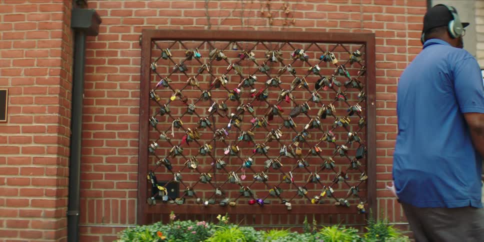 A delivery worker pushes boxes past a padlocked fence and brick wall