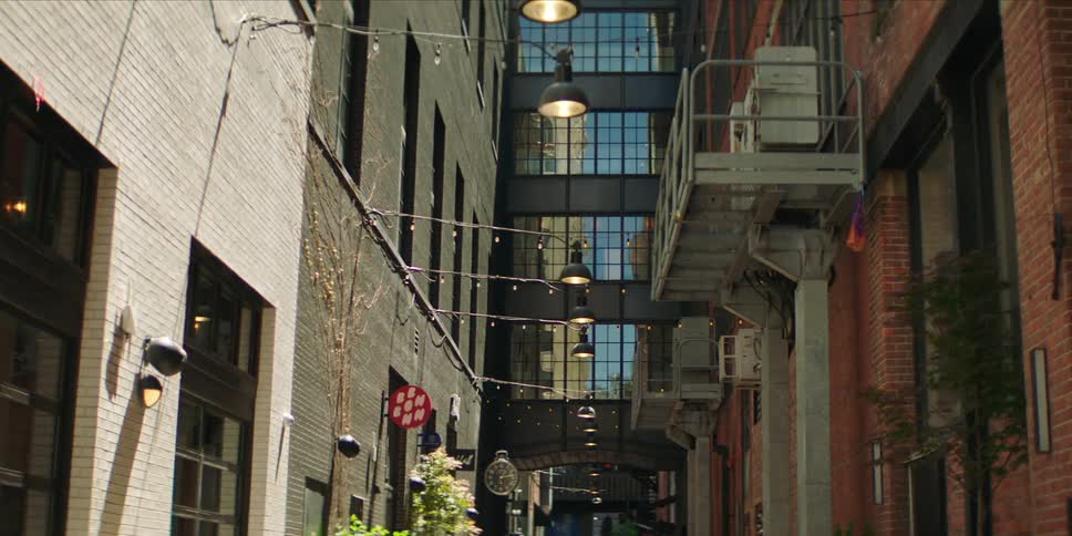 Narrow urban alleyway between tall brick buildings lit by hanging string lights and industrial lamps