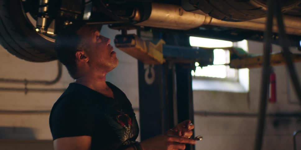 Car mechanic works on a car lifted by a frame while at the garage