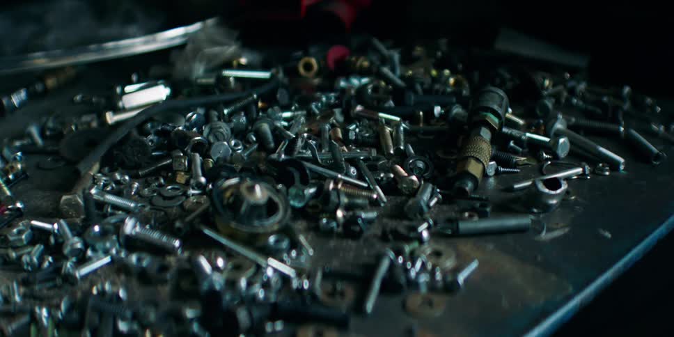 Bolts and other fasteners cover a dusty surface near a couple of boxes