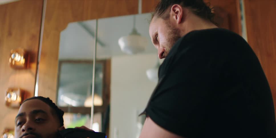 A barber trims a smiling mans beard with a trimmer inside a salon