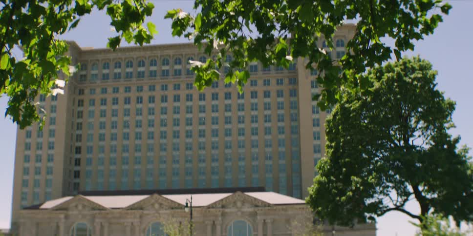A tall historiclooking stone building stands behind a parklike area with trees and cars