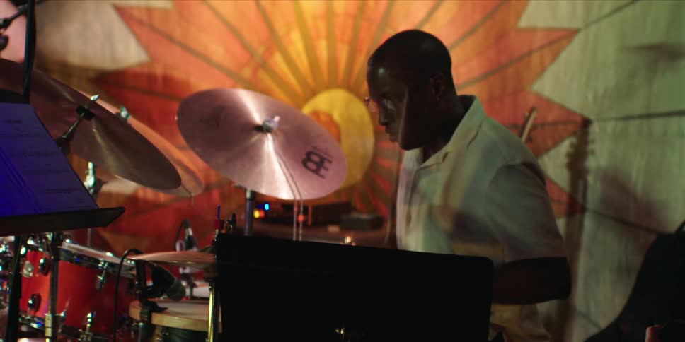 Male drummer plays the drums while someone stands nearby