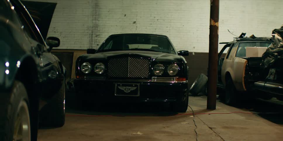 A luxury bentley car is parked inside a dimly lit garage facing the camera