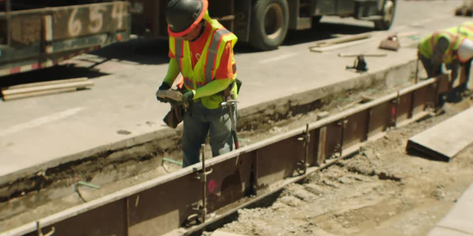 Construction workers wearing safety gear work on a road construction site under bright sunlight