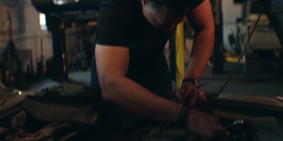 A mechanic working on a car engine with the hood open inside a workshop at midday