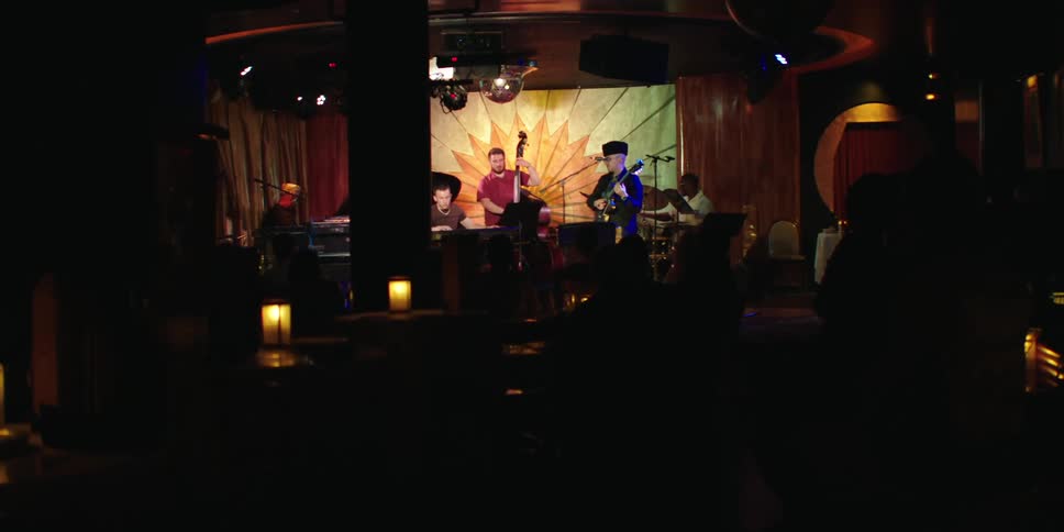 A band of musicians perform under lights on a stage at a social gathering at night