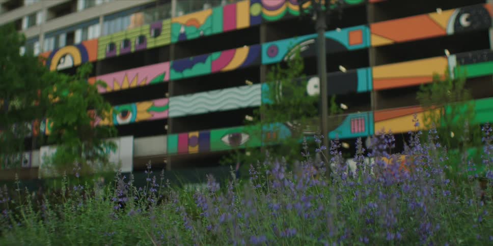 Lavender flowers are outside the building with a mural painting on the side