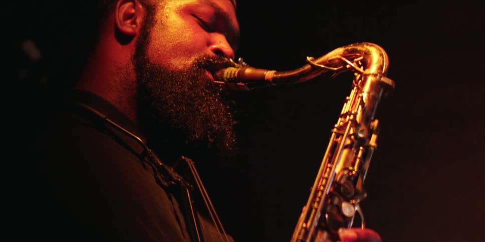 A man passionately playing a saxophone under warm stage lighting