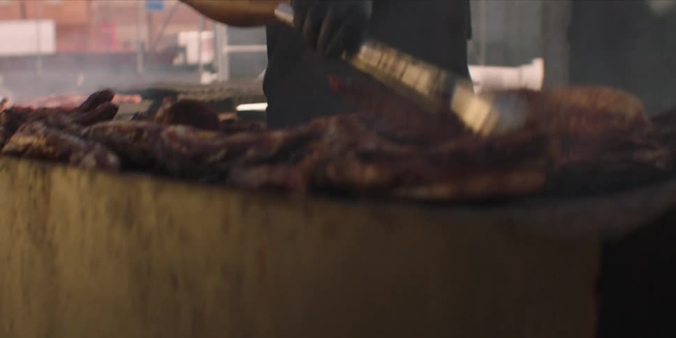 Black cook grills meat at an outdoor grill in daytime