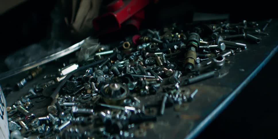 A series of bolts and nuts are placed on a steel desk in a mechanic workshop