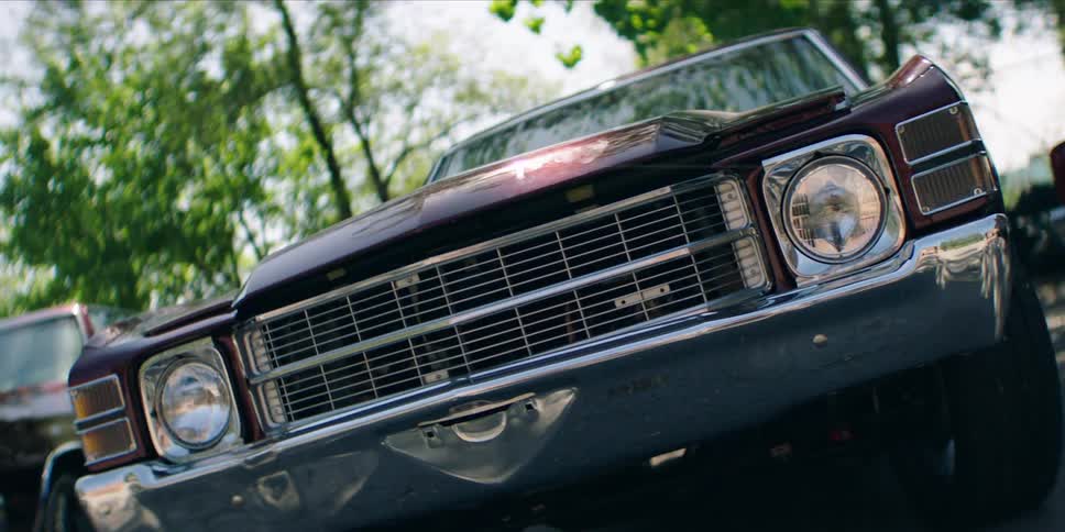 A chevrolet el camino is parked in a parking lot surrounded by trees at midday
