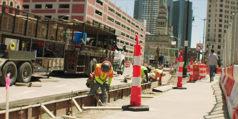 Pedestrians walk past a crew working on the road in the city on a sunny day