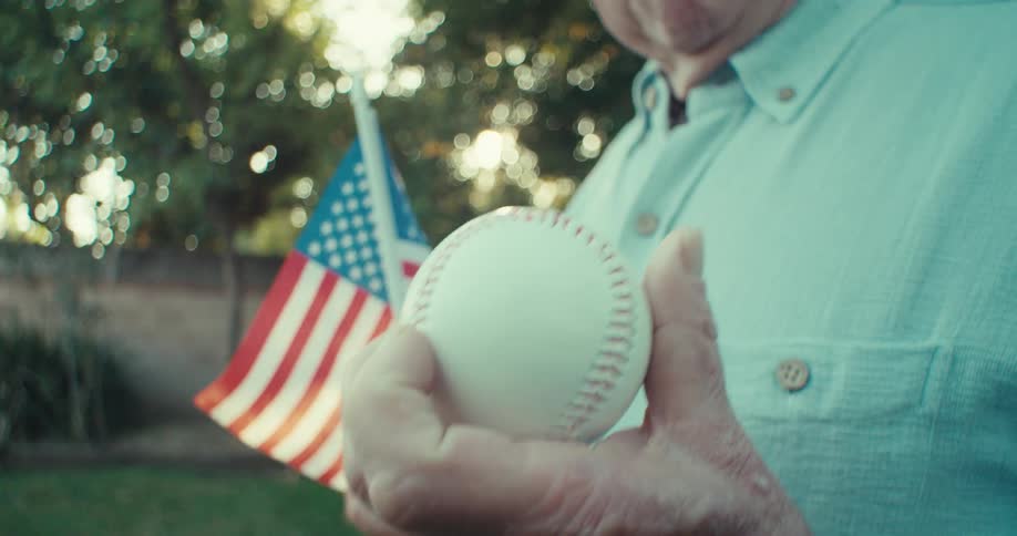 Old man in backyard smiles at ball in hand holding american flag