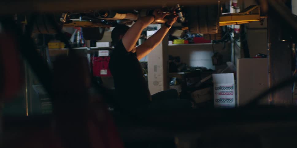 A mechanic lying on a creeper beneath a car inside an auto repair shop focused on fixing the vehicle