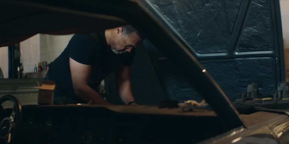 A man repairs a car engine in a dimly lit garage