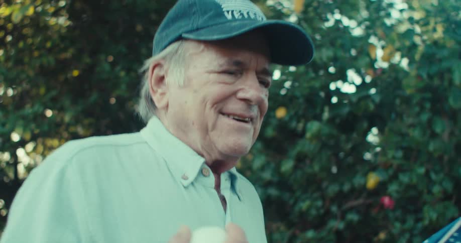 Elderly man holding a baseball and walking outdoors