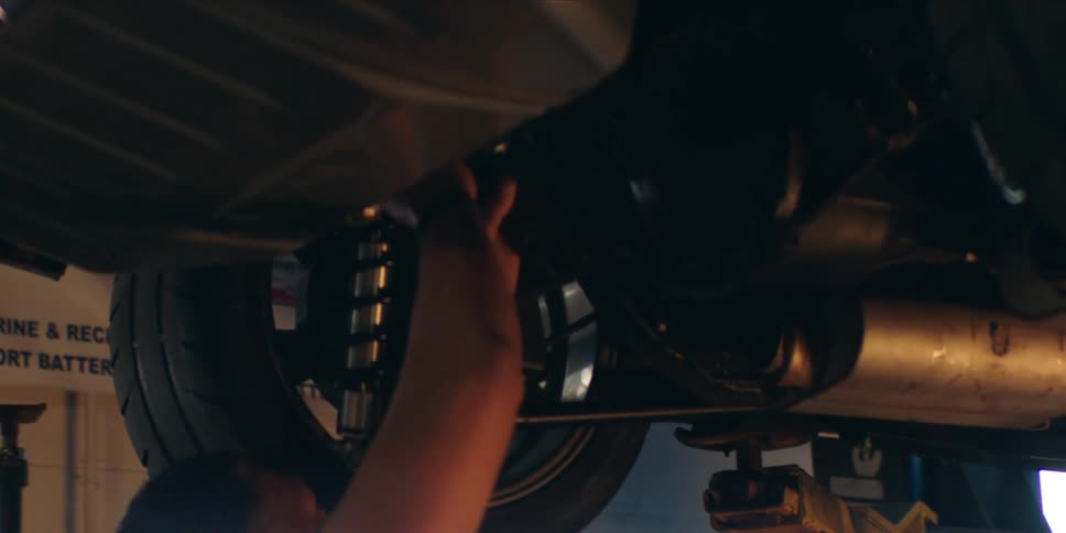 A mechanic stands under a car and repairs it in an auto shop
