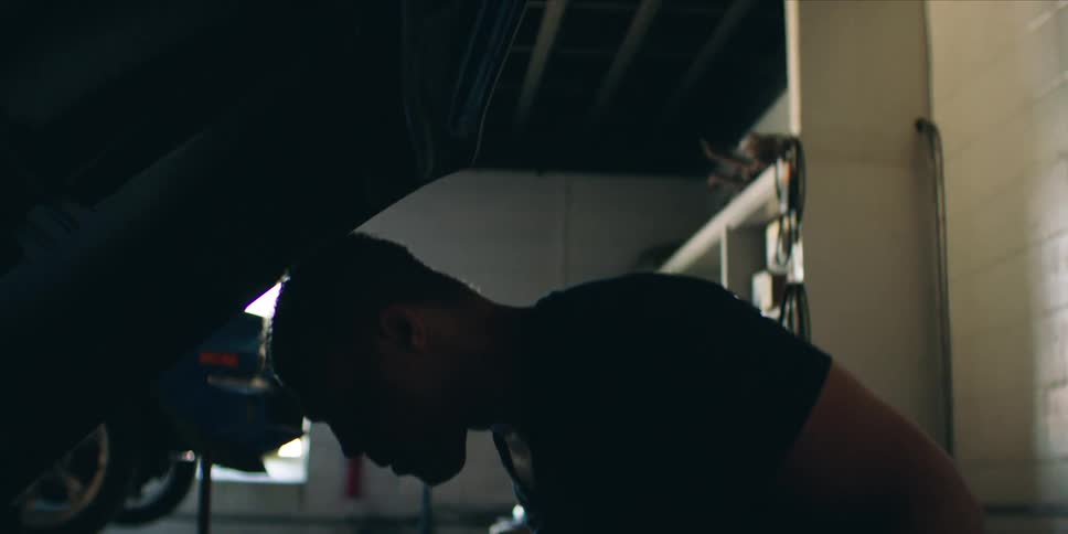 A mechanic is working on a car inside a garage focused on making repairs