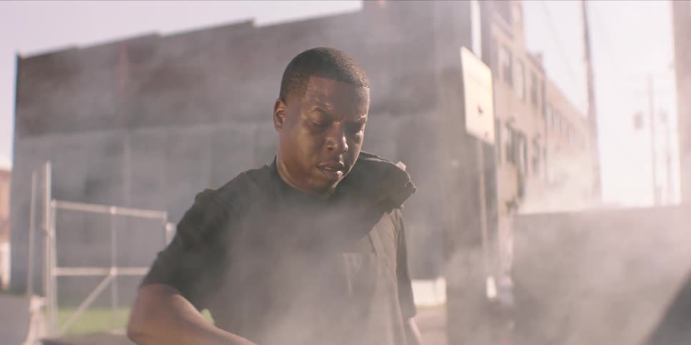 A black man cooks meat on a large outdoor grill on a sunny day