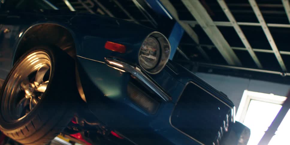 The exterior of a blue vintage car that is being lifted inside a garage