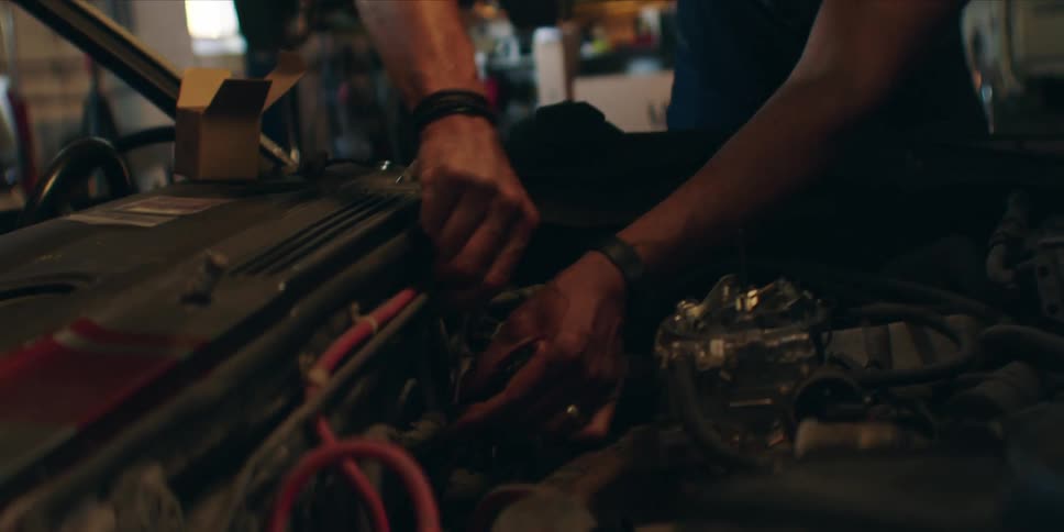 A mechanic fixes something under the hood of a car