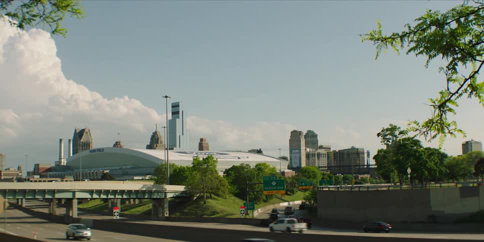 Several cars and trucks are driving on the highway near a city
