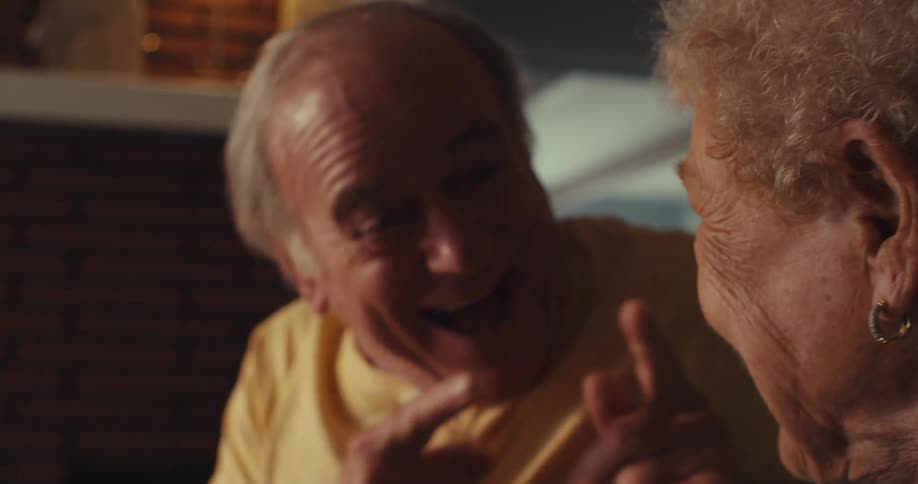 An elderly couple sits closely together sharing a warm affectionate moment indoors