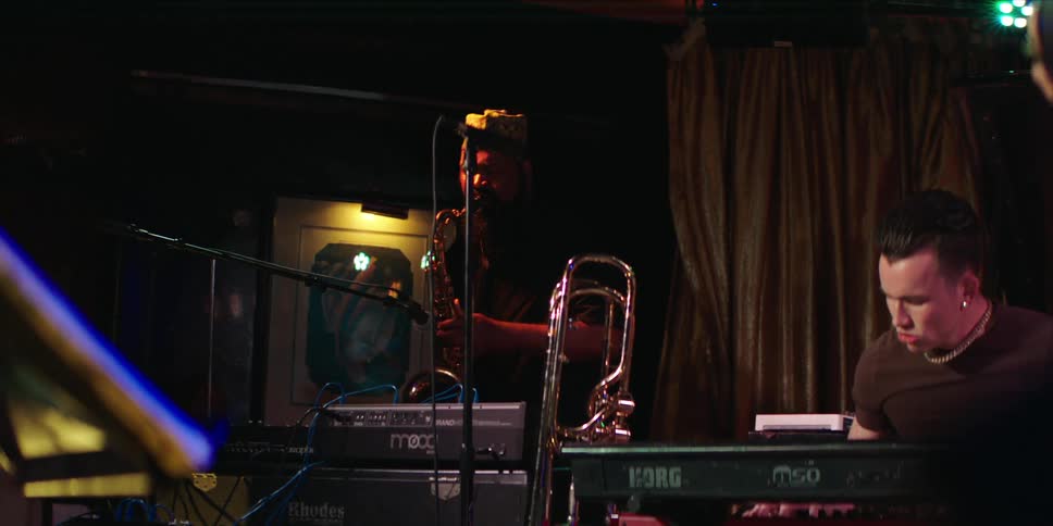 A jazz band performs live with a saxophonist and keyboardist under moody stage lighting