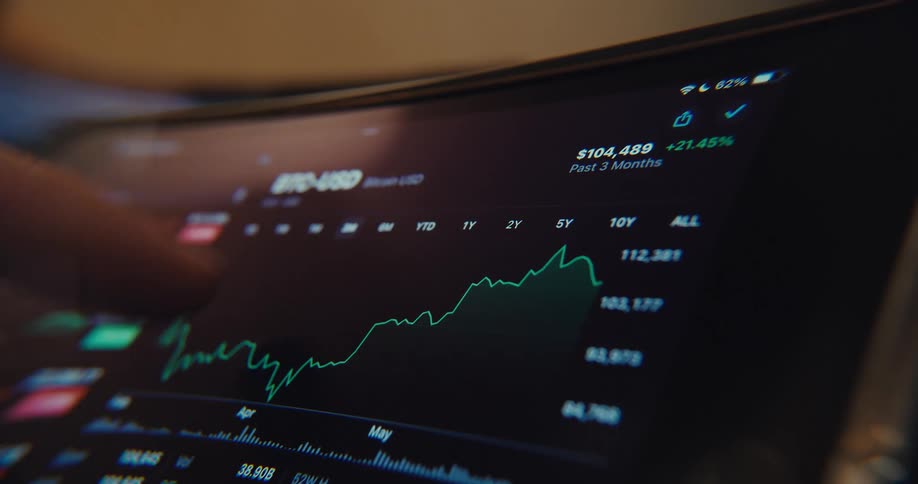 A finger points at a tablet screen displaying a fluctuating stock market graph