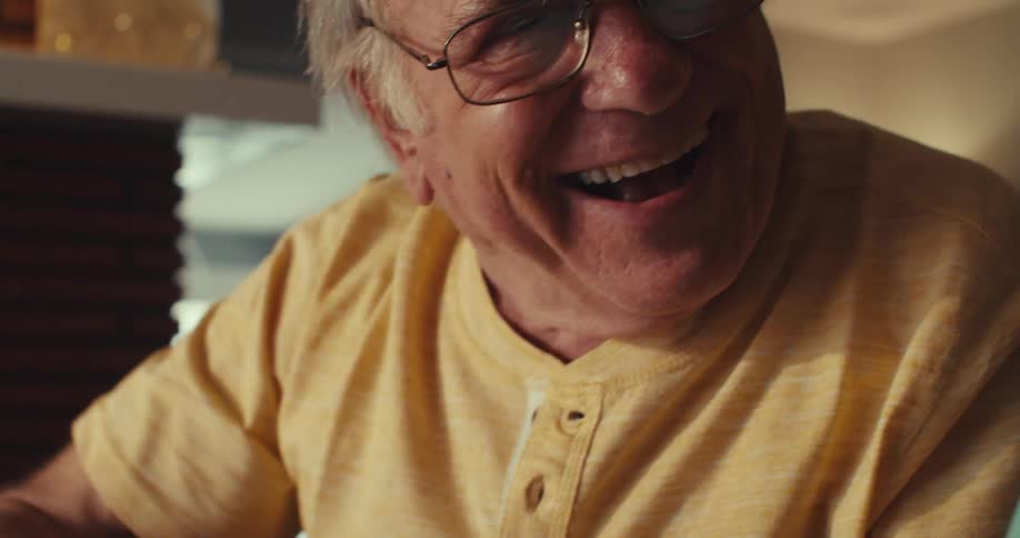 An elderly man jokes around with his wife by pretending to be a moose using his fingers as antlers