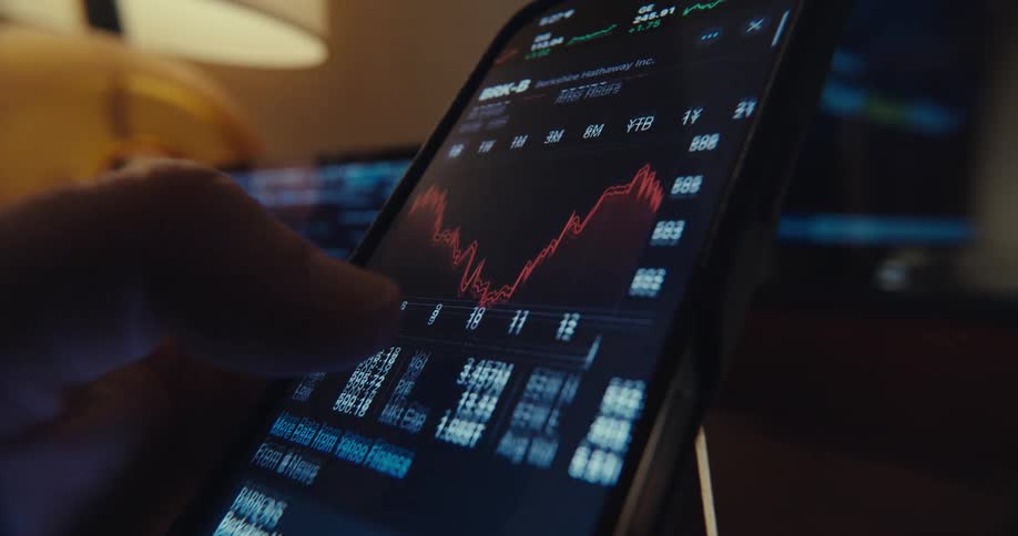 A man using his phone scrolling through news and looking at a financial stock chart