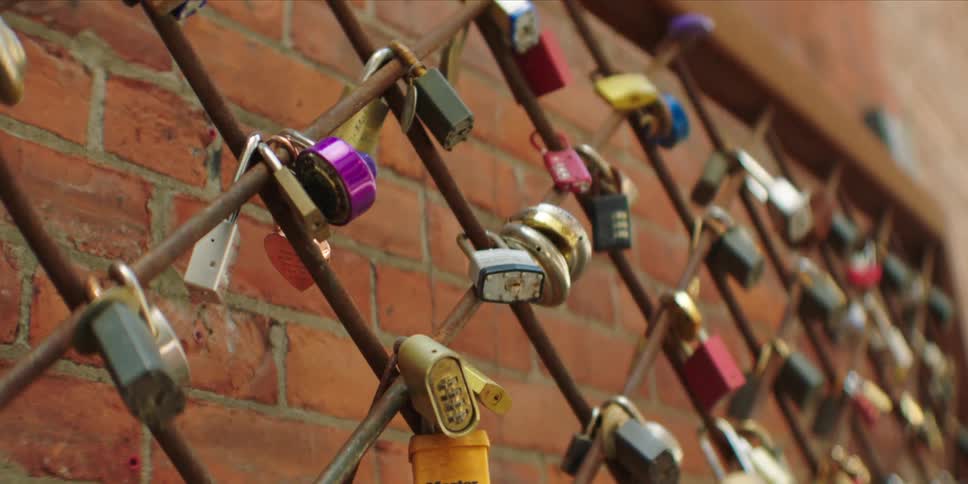Dozens of colorful padlocks are attached to a metal fence in front of a brick wall
