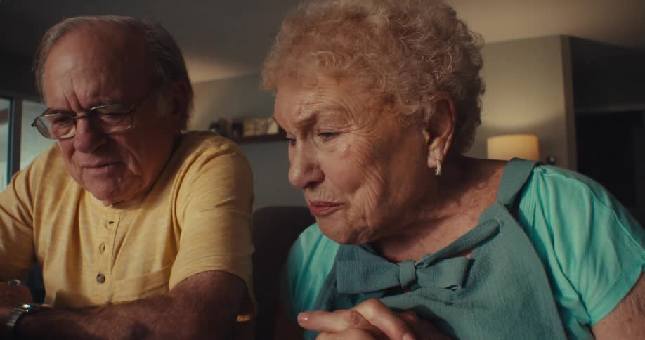 An elderly couple sitting at a table looking at something on the table and talking