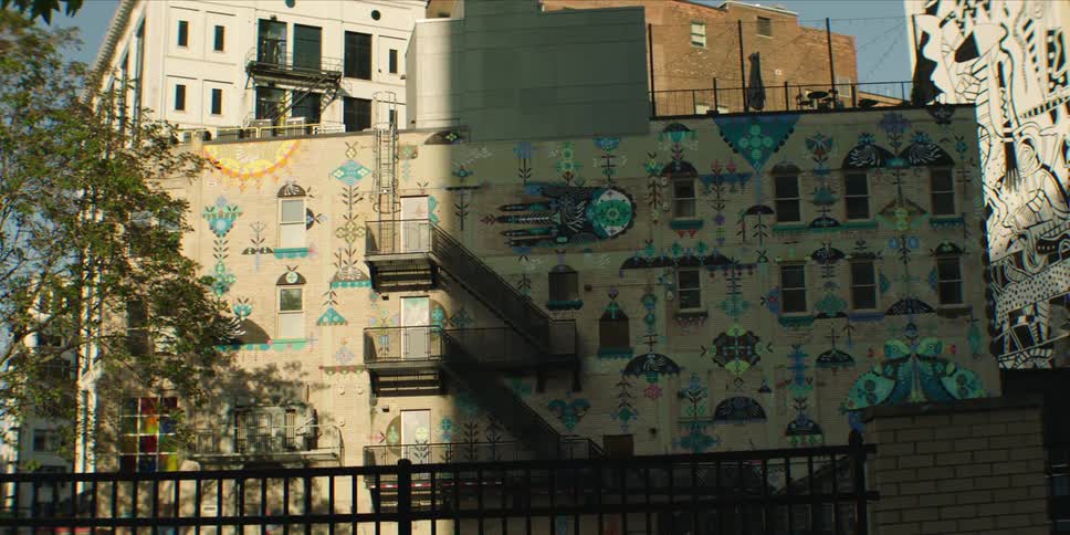 Colorful murals cover a city building wall with an exterior metal staircase