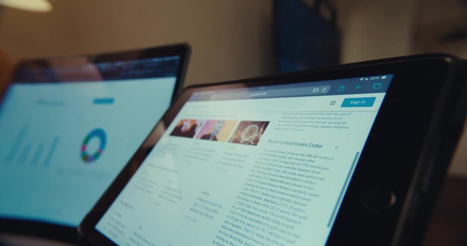 Close up of a tablet screen and laptop screen on a table displaying a scrolling web page and data analytics respectively
