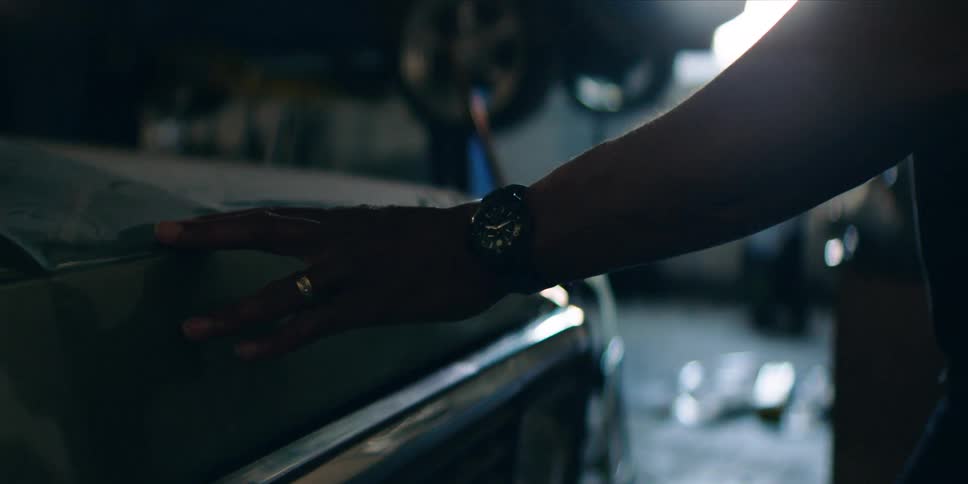 A man runs his hand across the hood of a truck in a garage
