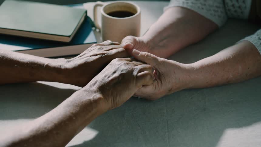 Two people hold hands with a cup of coffee nearby