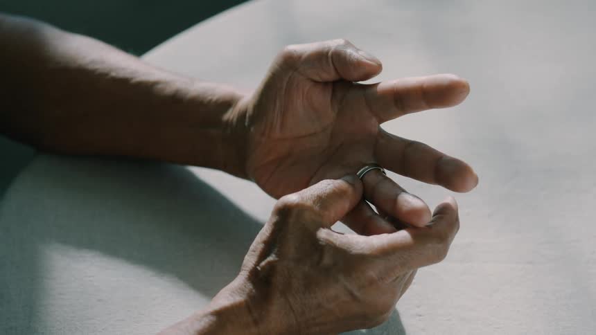 A pair of hands is shown in closeup with one hand playing with a ring from a finger of the other hand