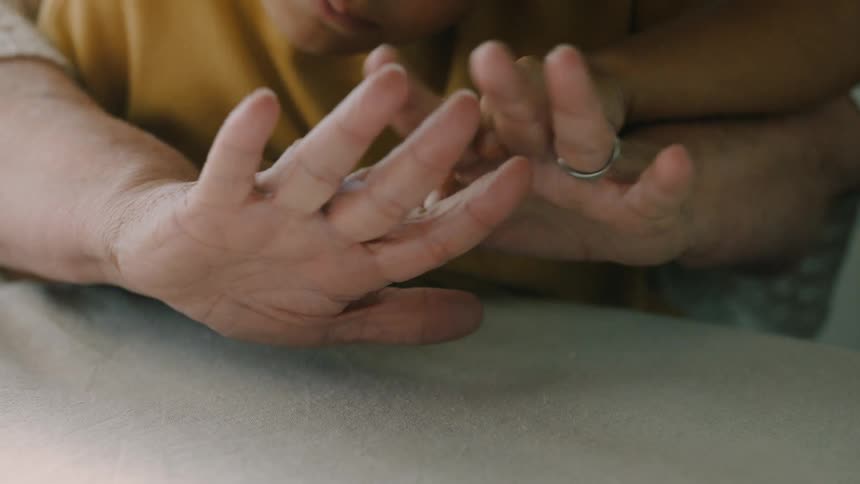 A childs hand touching an elderly mans hand with a ring on his finger and turning his palms upwards