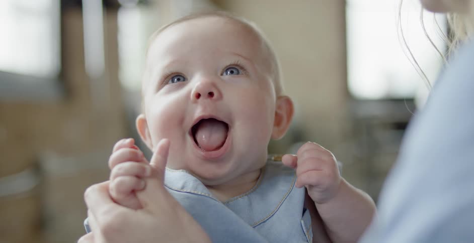 A baby smiles and licks a woman's hand