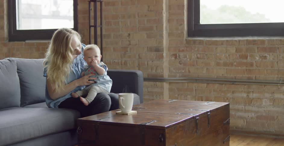 A woman holds a baby on a living room couch
