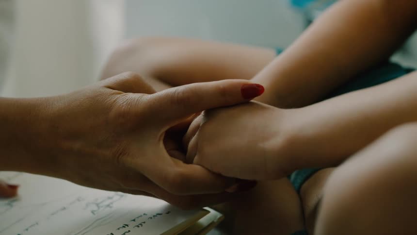 A childs hands touching their fingers and then an adult hand with red nails caresses the childs hands