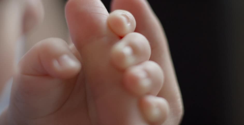 A baby wraps its fingers around a person's finger