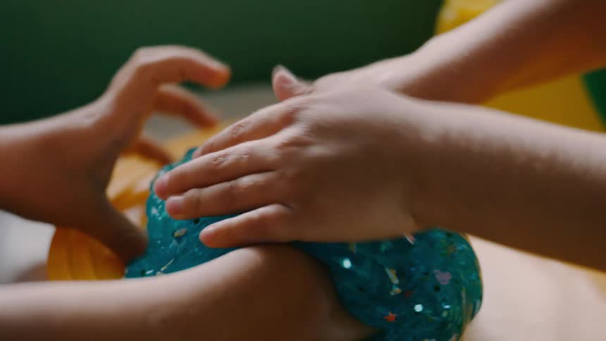 A kid wraps blue slime around another kids arm as they both laugh and play