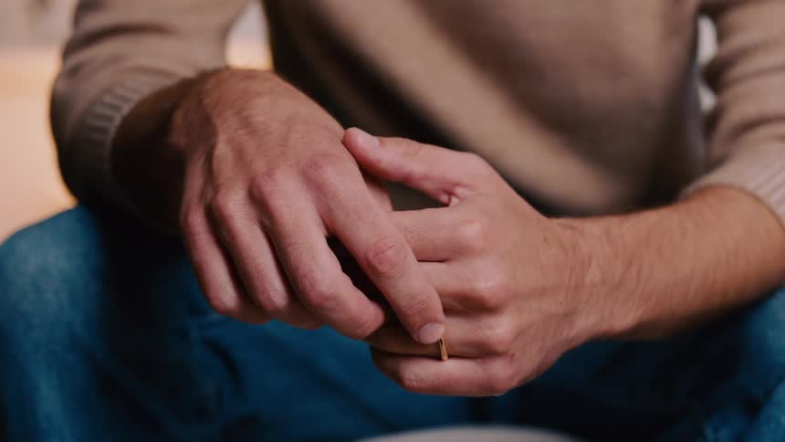 Hands of an anxious man sitting down fidgeting with his wedding ring