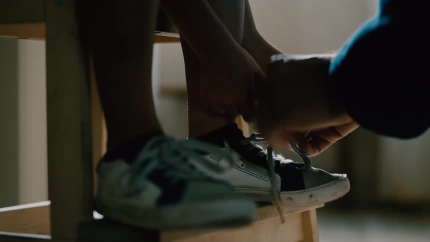 Closeup of a mans hands tying the shoelace on a little boys shoe