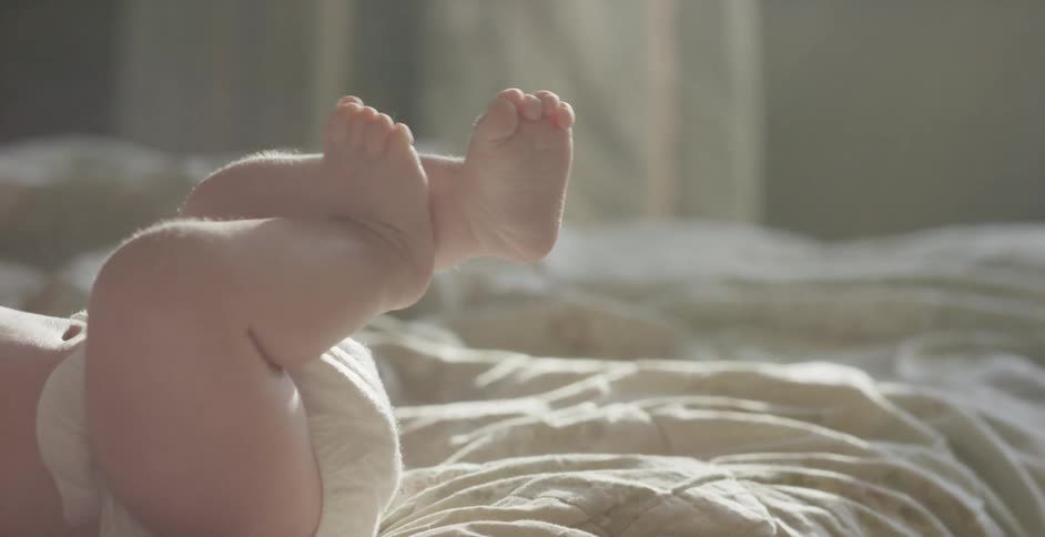 A baby lies on a bed as sunlight streams through the window