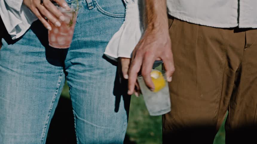 Closeup of a womans hand approaching and holding hands with a man who is holding a glass of drink