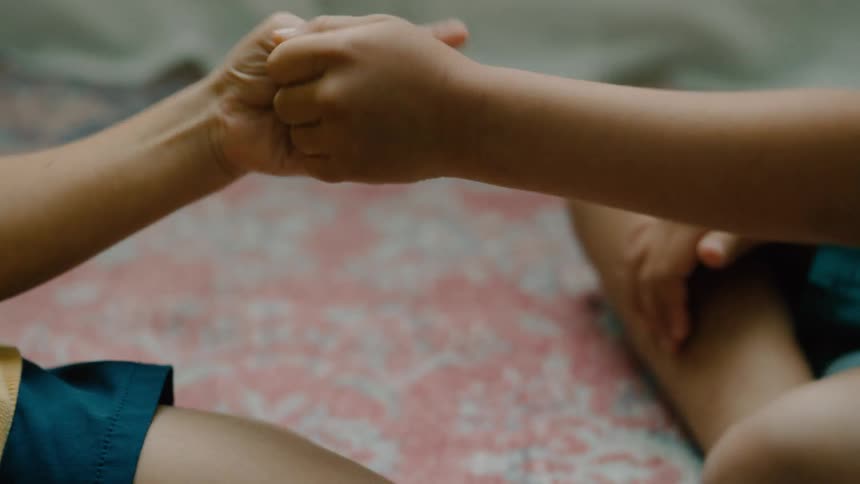 Two kids hold hands while playfully engaging in a thumb war game